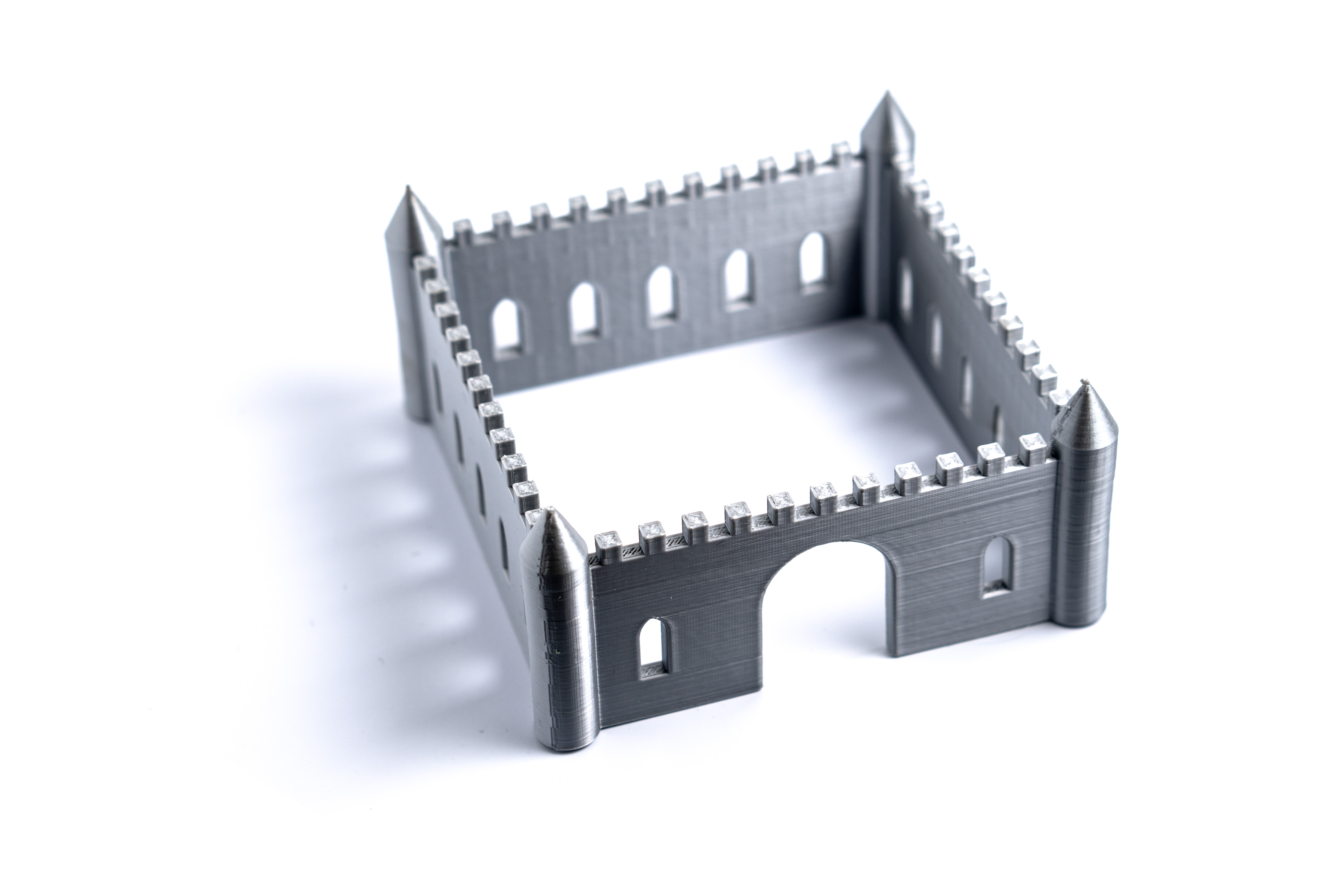 A square castle with turrets at each corner, a rounded main door, and Gothic arch windows all around. Crennelations are arranged all around the top of each wall.